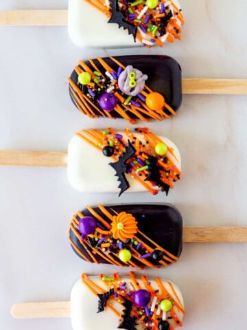black and white Halloween cakesicles decorated with orange chocolate drizzle and Halloween sprinkles