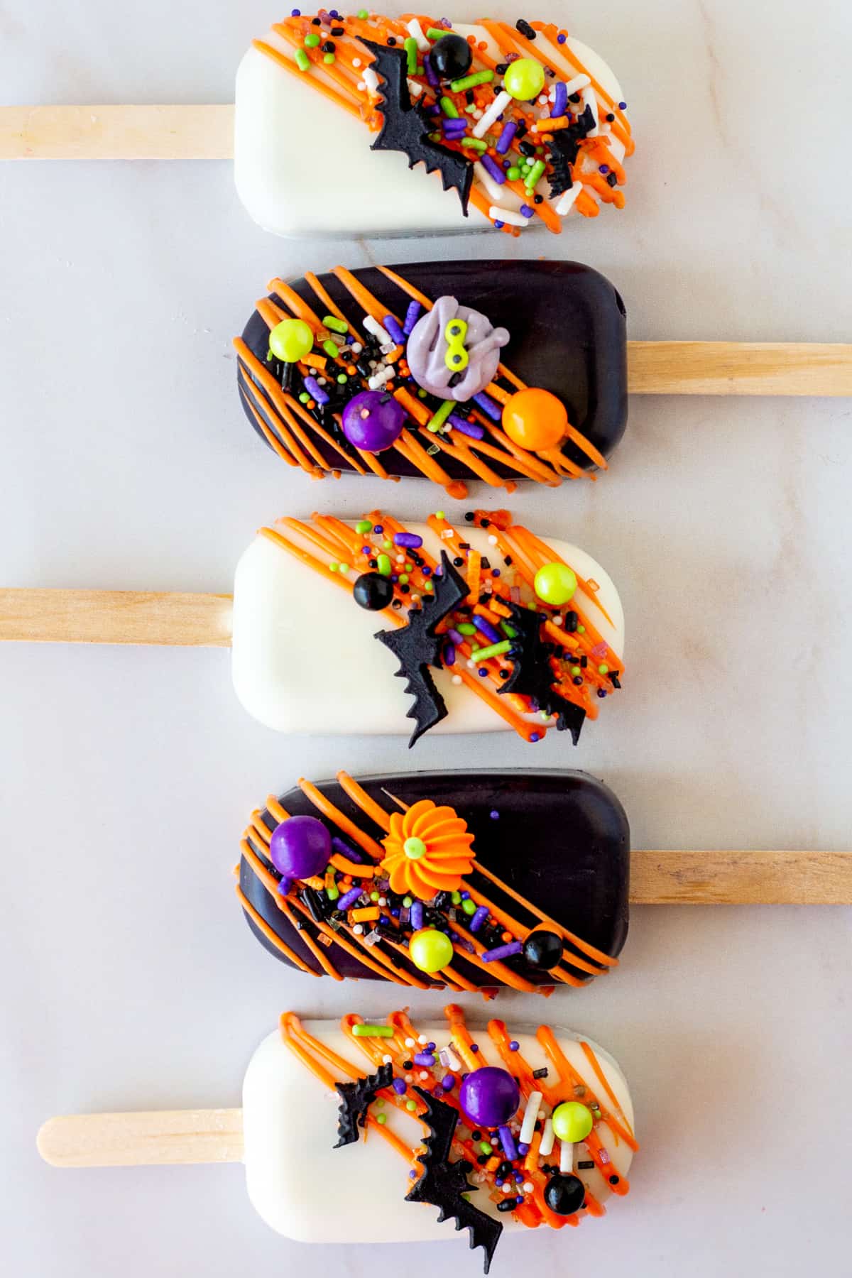 black and white Halloween cakesicles decorated with orange chocolate drizzle and Halloween sprinkles