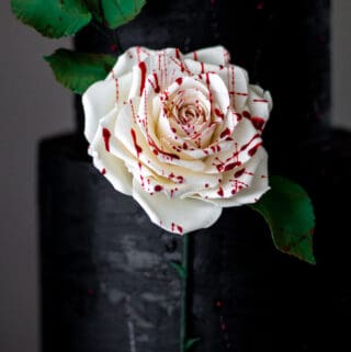 side view of black ganache cake with edible fake splattered gum paste rose