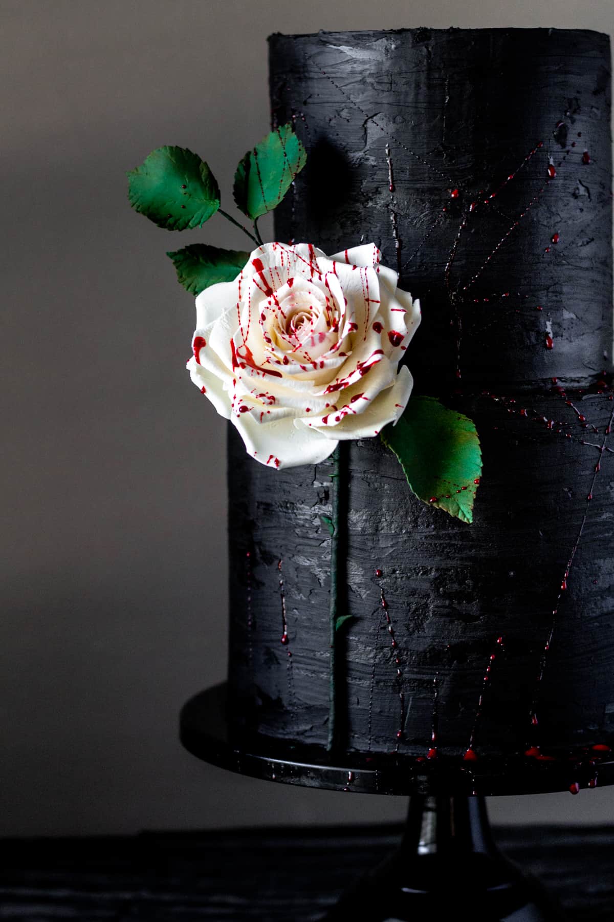 side view of black ganache cake with edible fake splattered gum paste rose