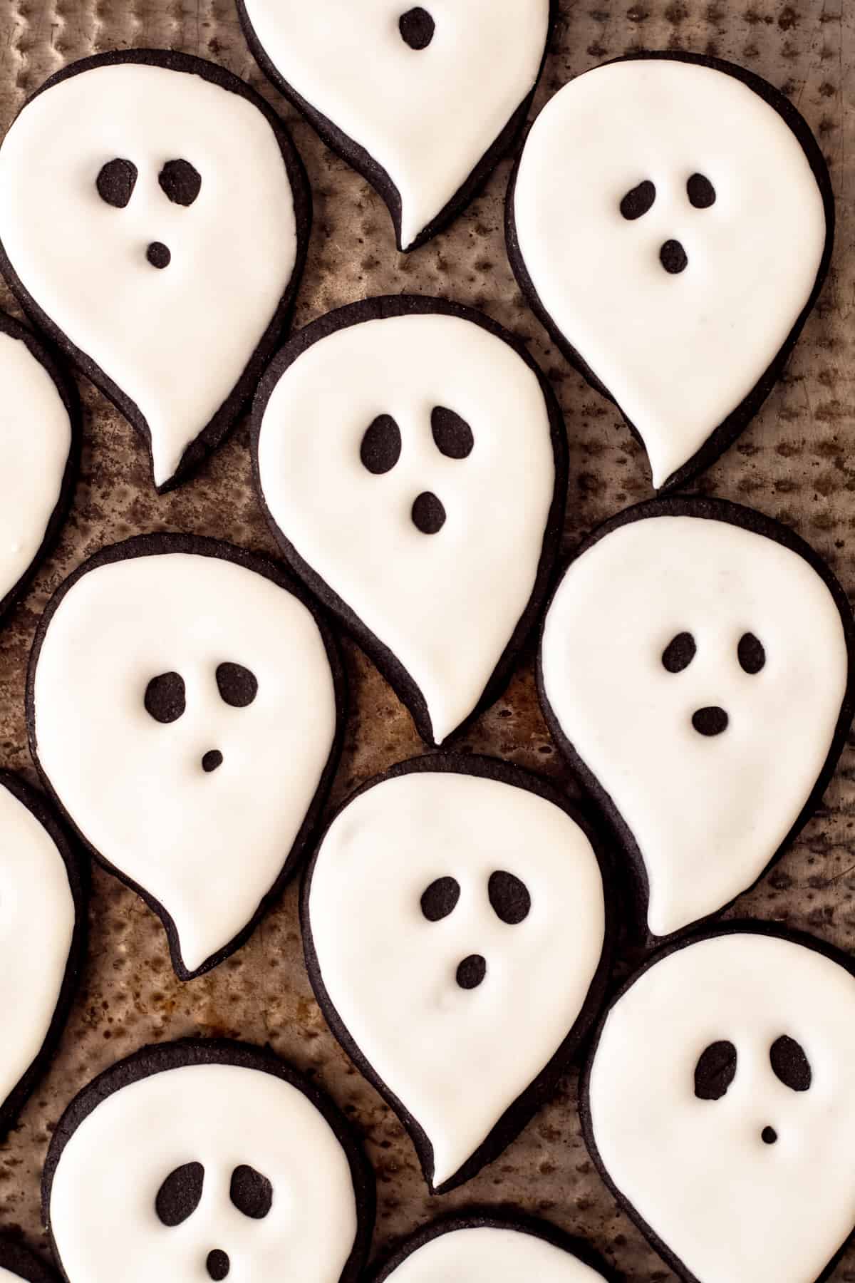 pan full of black cocoa cut out sugar ghost cookies decorated with white royal icing