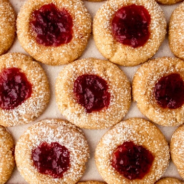 cranberry chai thumbprint cookies lined up on a cookie sheet with powdered sugar sprinkled on top