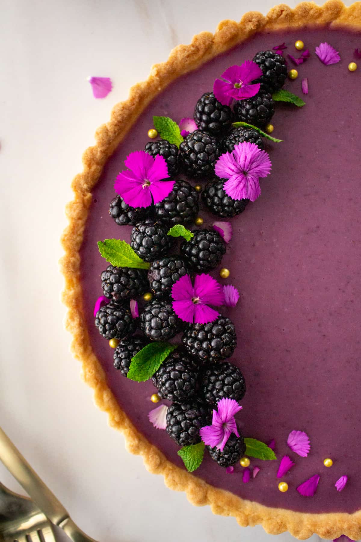 close up shot of tart decoration of blackberries, mint, blossoms and gold pearls